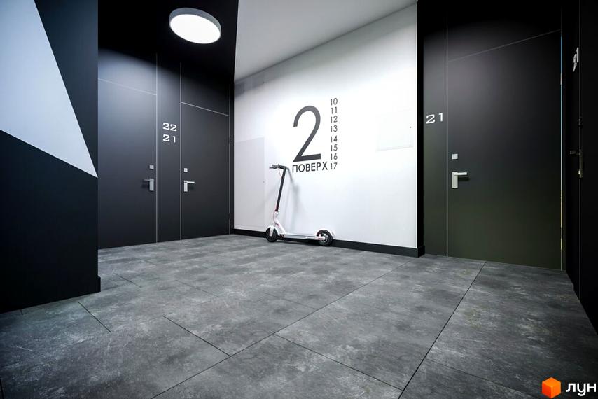 Сучасний інтер'єр холу житлового комплексу OBRIY3 з дверима та нумерацією поверхів. Біля стіни стоїть електросамокат.
