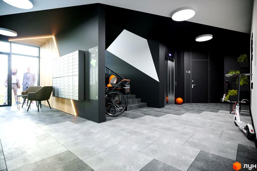 Сучасний дизайн вхідної групи ЖК OBRIY3 з поштовими скриньками, місцями для зберігання самокатів та зоною відпочинку. Оздоблення стін та підлоги виконано в сірих тонах з дерев'яними акцентами.