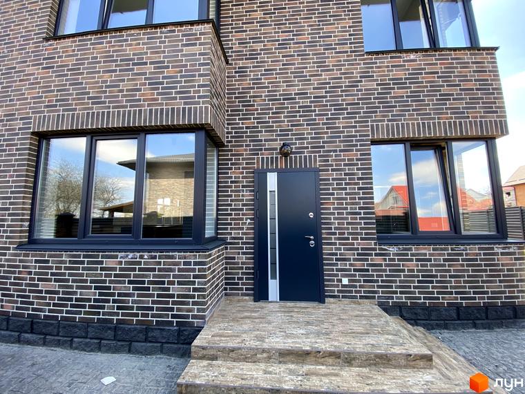 Фасад будинку Котеджного містечка Весняний з темно-коричневої цегли, великі вікна. Вхідні двері та сходи з бруківки.