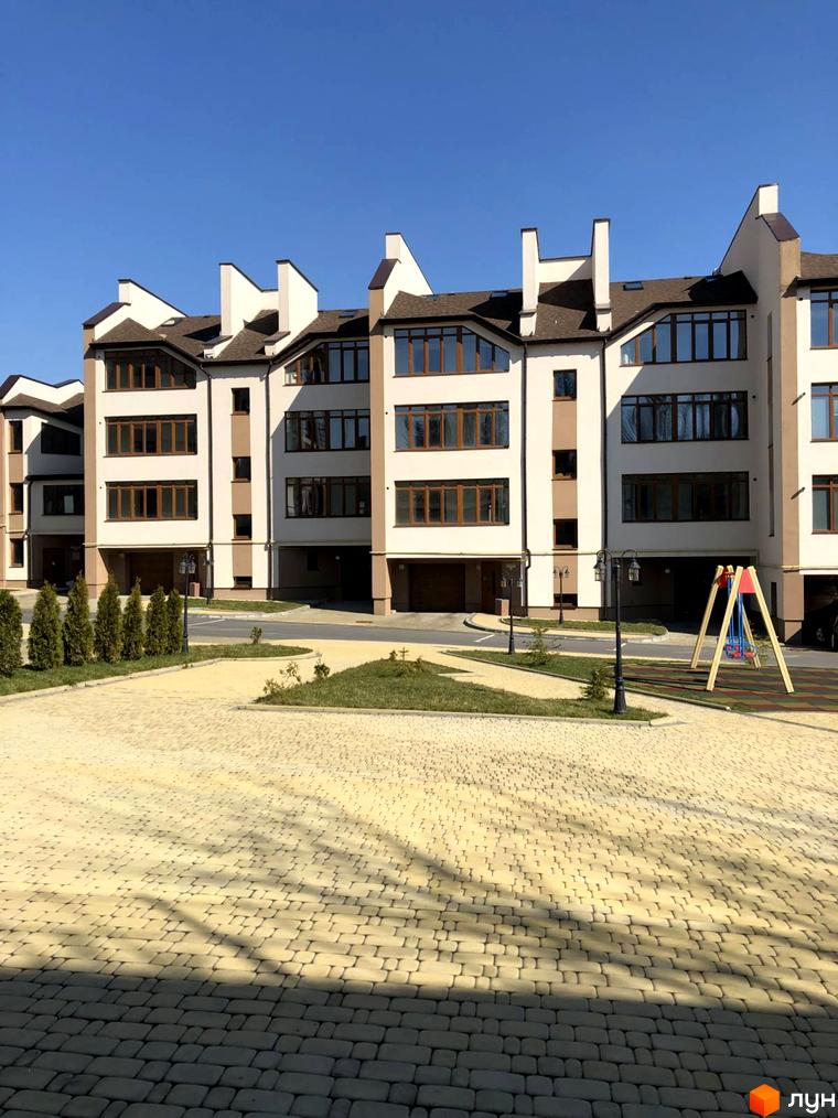 Новобудова на вулиці Паневежиській (Пугачова), 2, з бруківкою та дитячим майданчиком. Зовнішній вигляд будинку з коричневим дахом та великими вікнами.