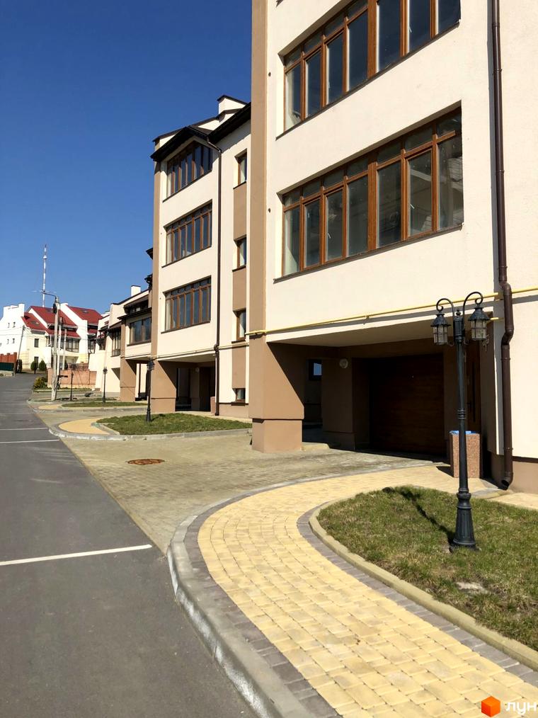 Зовнішній вигляд житлового комплексу на вул. Паневежиська (Пугачова), 2, з елементами фасаду бежевого та білого кольору, великими вікнами та прибудинковою територією з бруківкою та газоном.