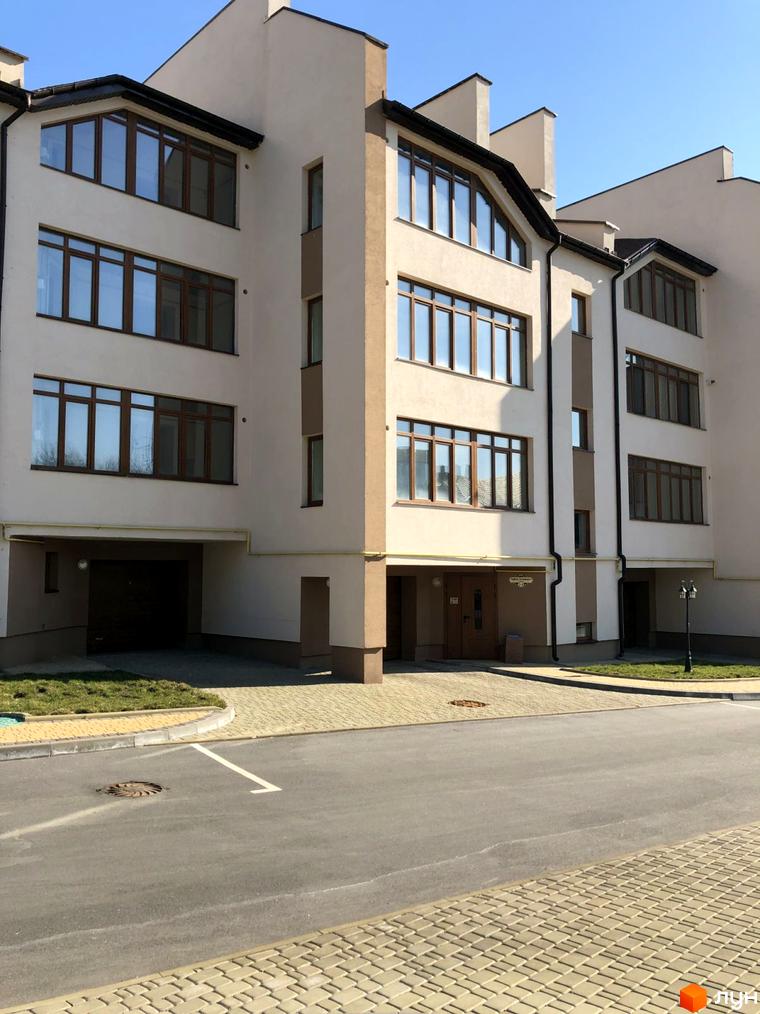 Фасад житлового комплексу вул. Паневежиська (Пугачова), 2, з великими вікнами та прибудинковою територією з бруківки та зеленими насадженнями.