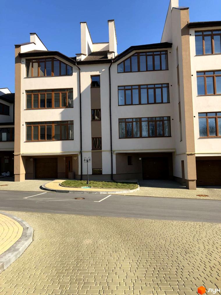 Новобудова на вул. Паневежиська (Пугачова), 2 з білим фасадом, коричневими вікнами та гаражами. Прибудинкова територія має бруківку та зелені насадження.