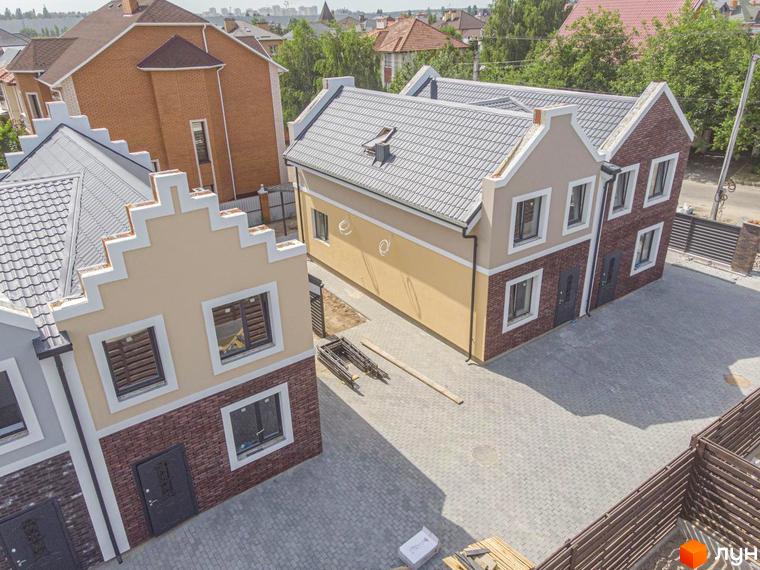Зображення Дуплексів Lucky Home з двоповерховими будинками, оздобленими світлою штукатуркою та цеглою, з сірими дахами. Прибудинкова територія вимощена бруківкою.