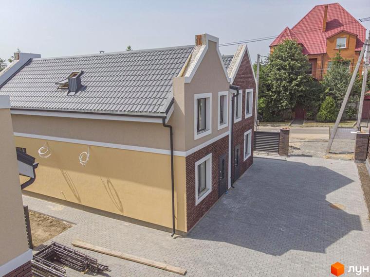 Дуплекси Lucky Home: двоповерхові будинки з сірим черепичним дахом та цегляними фасадами, розташовані на вимощеній сірою плиткою прибудинковій території.