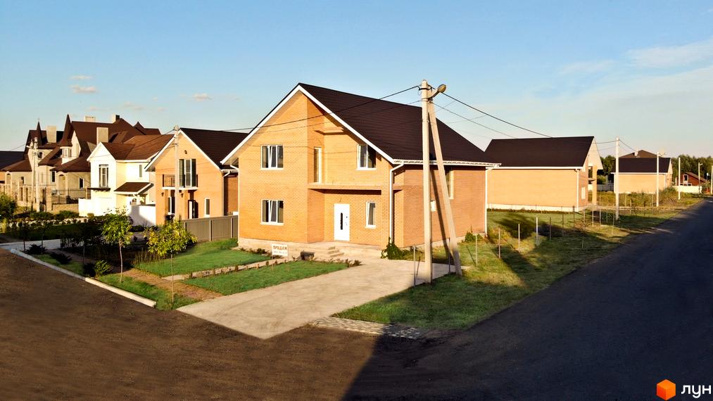 Котеджне містечко КМ Зоряний: цегляні будинки з темними дахами та зелені газони. На території новобудови є доглянуті дерева та доріжки.