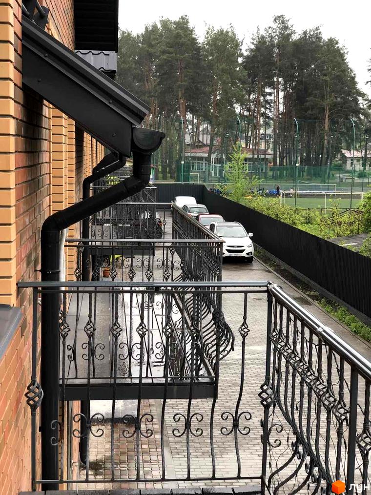 Таунхауси Classic Nova з цегляним фасадом та кованими балконами на тлі зеленої зони з деревами та спортивним майданчиком.