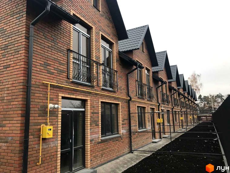 Зовнішній вигляд таунхаусів Classic Nova з цегляним фасадом та чорним дахом. Прибудинкова територія з доріжками та паркувальними місцями.