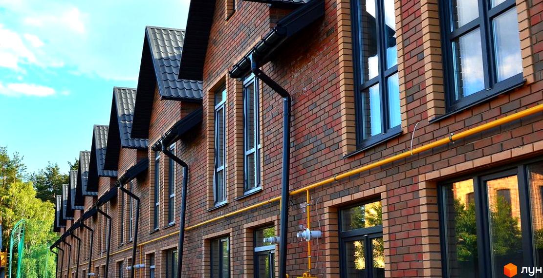 Таунхауси Classic Nova - цегляні будинки з темними вікнами та дахами, розташовані поруч із зеленими деревами.