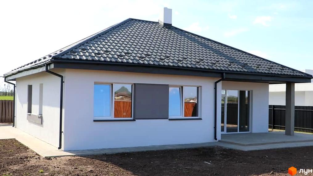 Зовнішній вигляд одноповерхового будинку з сірим дахом та білими стінами в КМ Лісне. Прибудинкова територія з зеленими насадженнями та парканом.