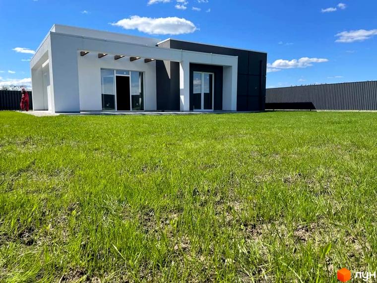 Котеджне містечко КМ Лісне: будинок з білою та сірою обробкою та великими вікнами на тлі зеленого газону та паркану.