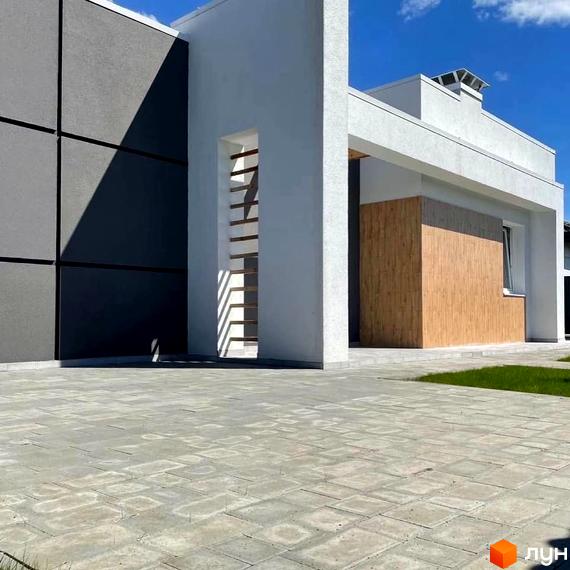 Котеджне містечко КМ Лісне: фасад будинку з сірими та білими елементами, дерев'яною вставкою та вимощеною сірою плиткою прибудинковою територією.