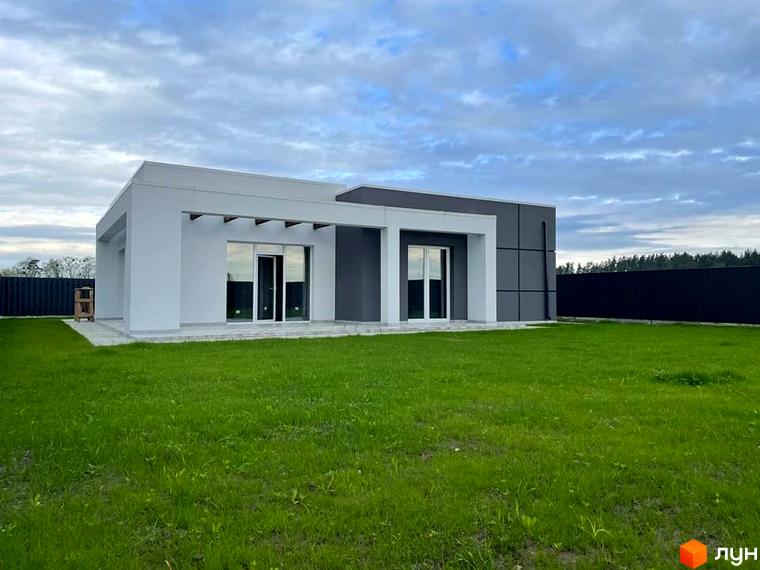 Котеджне містечко КМ Лісне: одноповерховий будинок з великими вікнами та сірою обшивкою, на тлі зелений газон та хмарне небо.