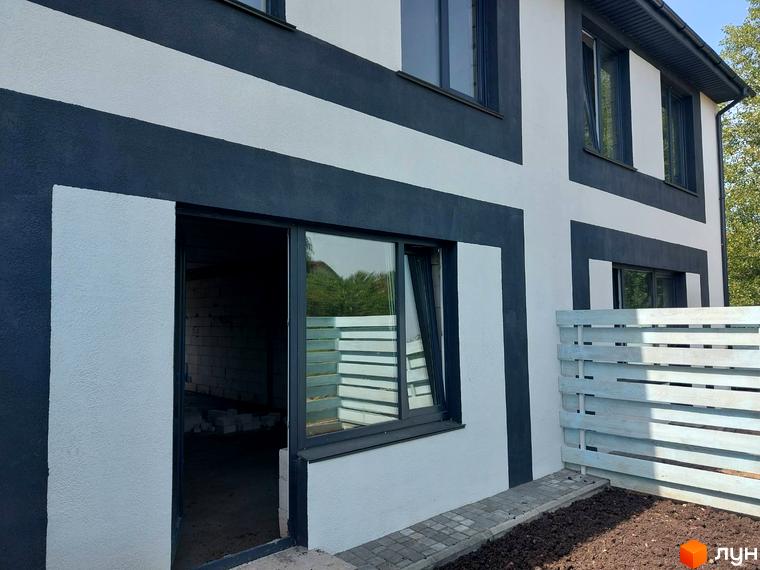 Таунхаус Sanny House з біло-темно-сірими фасадами та великими вікнами, поруч дерев'яний паркан та доглянута ділянка.