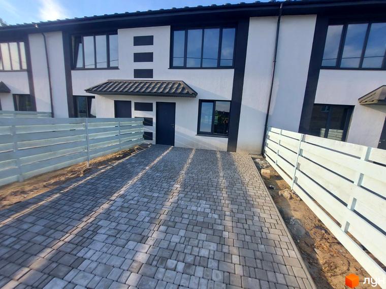 Таунхаус Sanny House з біло-чорним фасадом та бруківкою перед входом. Прибудинкова територія огороджена світлим дерев'яним парканом.