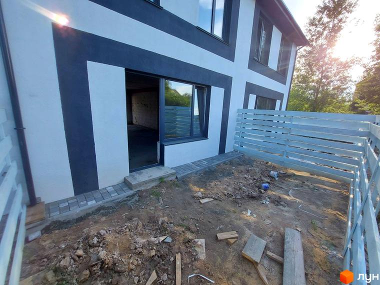 Таунхаус Sanny House з біло-сірим фасадом та великим вікном, що виходить на приватну територію з дерев'яним парканом.