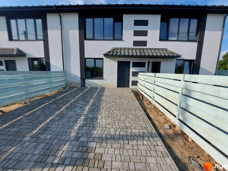 Таунхаус Sanny House з біло-сірим фасадом, вікнами та сірою бруківкою перед будинком. Поруч розташована дерев'яна огорожа.