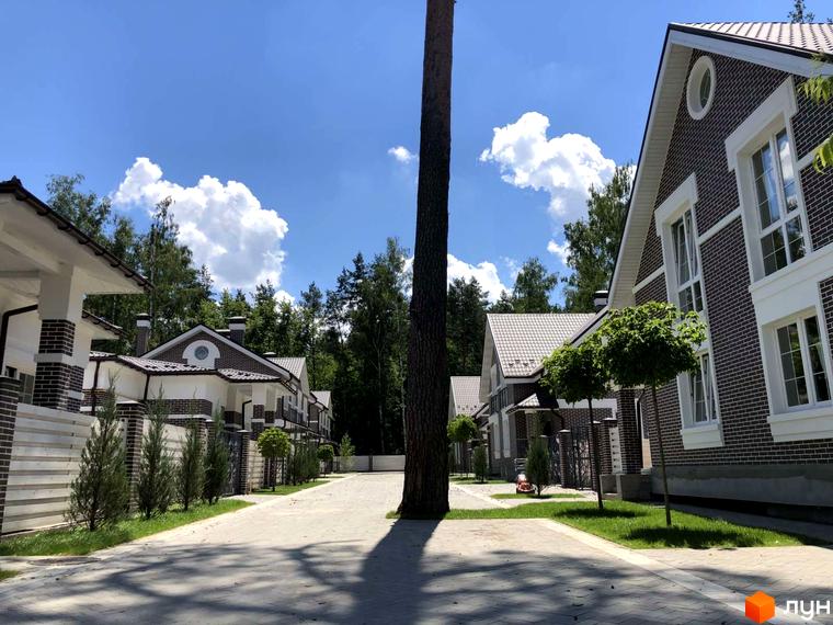 Містечко котеджів Dream Wood: будинки з темно-коричневої цегли, білими вікнами та коричневими дахами, оточені брукованими доріжками та зеленими газонами.