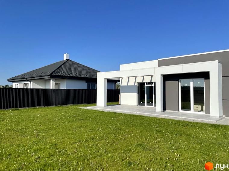 Котеджне містечко Лісне: сучасний будинок з великими вікнами та доглянутою зеленою територією. Навколо будинку огороджена ділянка з травою та парканом.