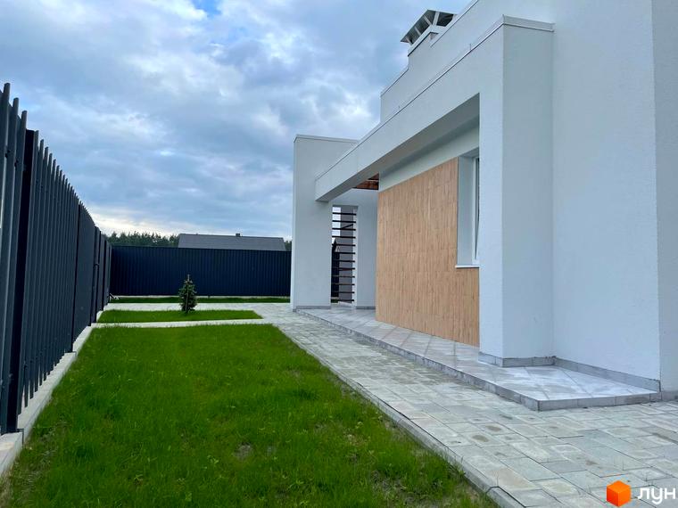 Котеджне містечко КМ Лісне: фасад будинку з дерев'яними елементами та прибудинкова територія з газоном і доріжками.