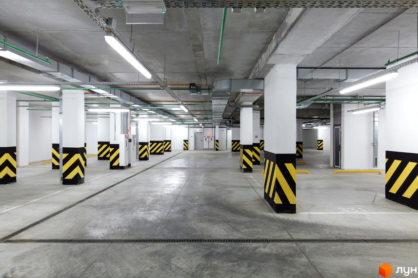 Паркінг житлового комплексу PecherSKY з просторими місцями для автомобілів та яскравими знаками безпеки.