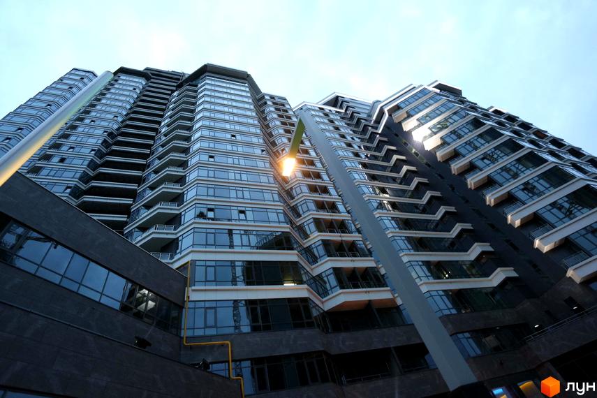 Житловий комплекс PecherSKY з сучасним фасадом та великими вікнами, прибудинкова територія з освітленням.