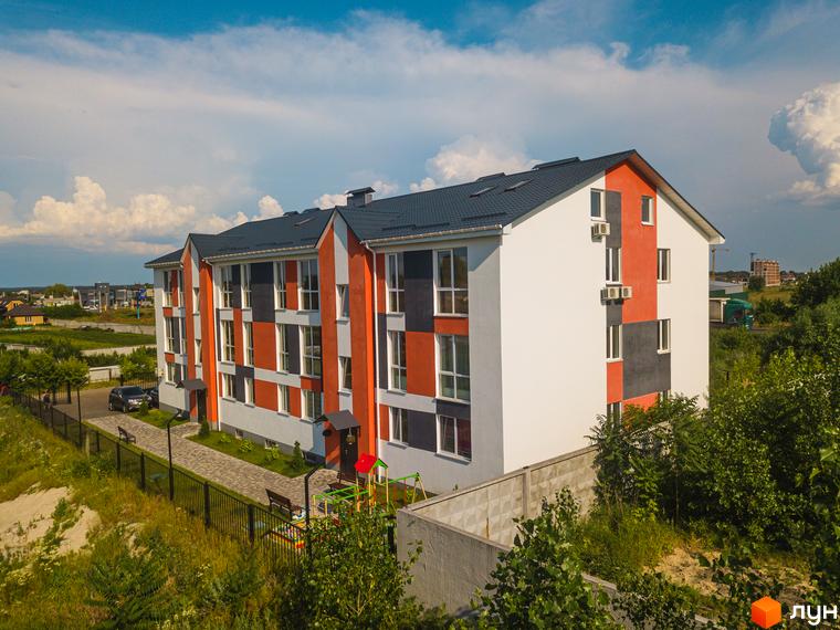 Зовнішній вигляд житлового комплексу Smart Format з фасадом у сірих та помаранчевих тонах, вікнами та кондиціонерами. На прибудинковій території розташований дитячий майданчик та лавки.