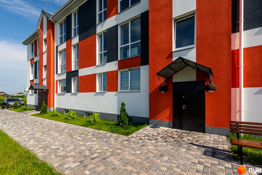 Новобудова ЖК Smart Format з яскравим фасадом та брукованою прибудинковою територією. Поруч зелена зона та лавка для відпочинку.