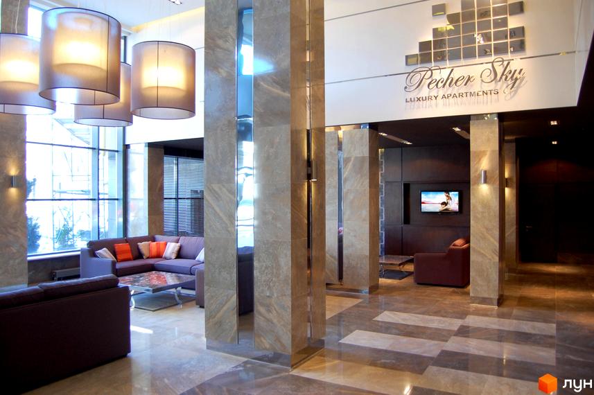 Сучасний хол житлового комплексу PecherSKY з великими вікнами та стильними меблями. Просторі зони відпочинку та елегантне освітлення.