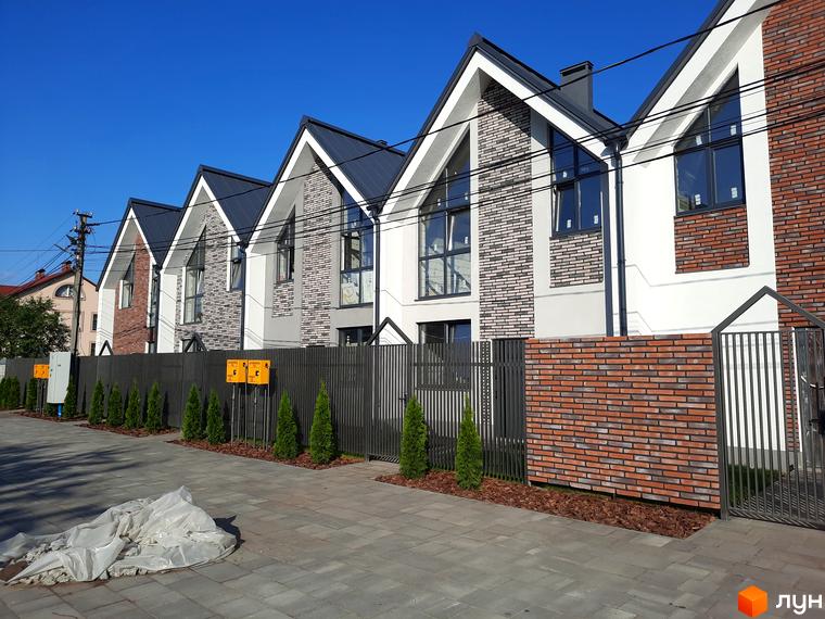 Зображення Котеджного містечка Villa Gatne: фасади будинків з цегли та великими вікнами, зелені насадження вздовж огорожі.