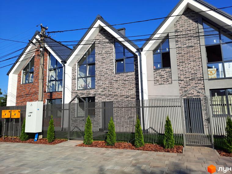 Зовнішній вигляд будинків Котеджного містечка Villa Gatne з великими вікнами та сірими парканами. Навколо будинків висаджені дерева.