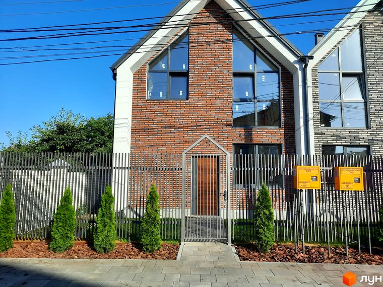 Зображення фасаду будинку в Котеджному містечку Villa Gatne з великими вікнами та металевою огорожею. Навколо будинку висаджені зелені насадження.