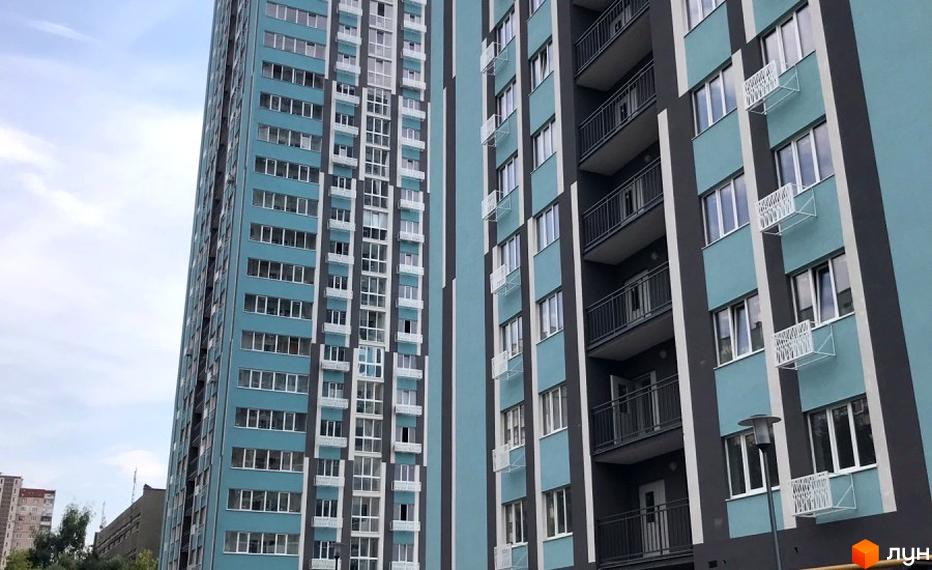 Зовнішній вигляд новобудови ЖК Журавли з блакитними фасадами та великою кількістю вікон. Будівельний проєкт з балконами та кондиціонерами.