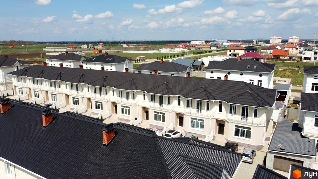 Котеджне містечко Дайберг: ряд світлих котеджів з темними дахами та балконами. Видно прибудинкову територію та зелені поля.