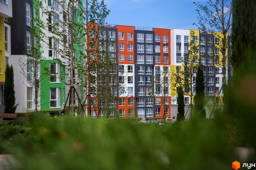 Житловий комплекс Синергія-3+ з яскравими фасадами та вікнами, оточений деревами та зеленню. Зовнішній вигляд будівель та прибудинкової території.