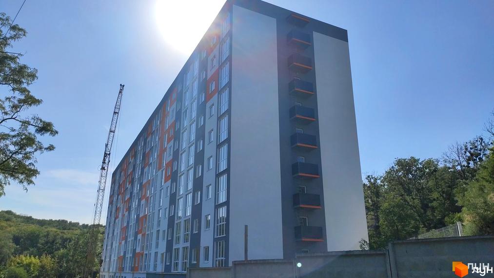 Зовнішній вигляд новобудови на вул. Піщана, 1б, з балконами та вікнами, на фоні блакитного неба та зелені.