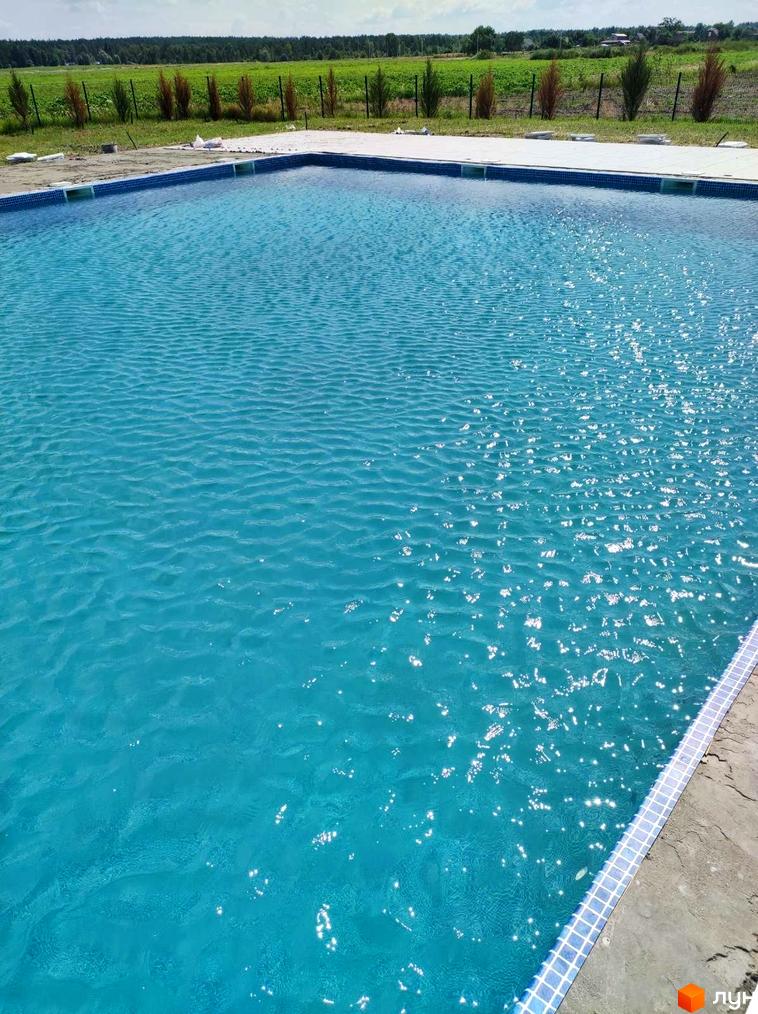 Басейн біля будинку в ЖК Лелека з блакитною водою та плиткою по краях. На фоні зелені насадження та небо.