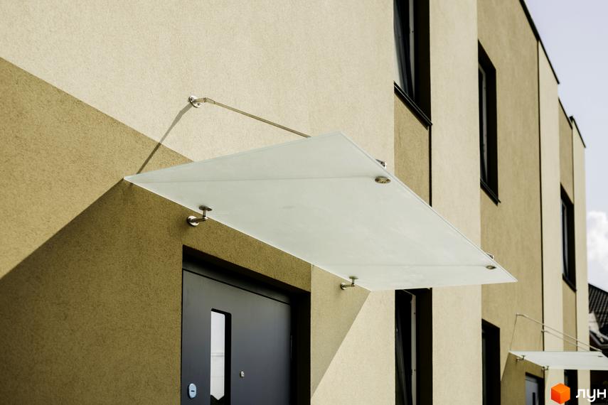 Сучасний вхід до будинку в житловому комплексі КМ My Land із скляним навісом. Зовнішній вигляд фасаду будинку.