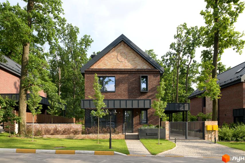 Котеджне містечко Oak Grove Town: двоповерховий цегляний будинок з темним дахом, вікнами та круглим візерунком на фронтоні. Прибудинкова територія з газоном та деревами.