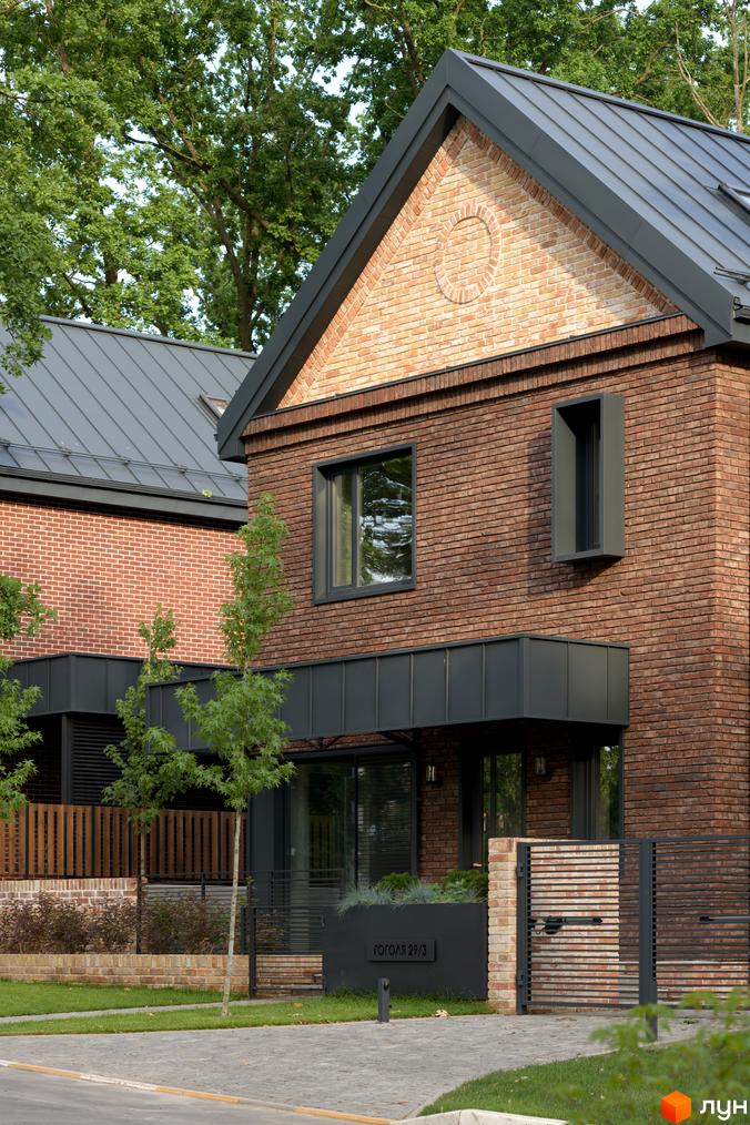 Зображення сторінки житлового комплексу КМ Oak Grove Town з цегляними будинками та металевим дахом. На території є газон, дерева та паркан.