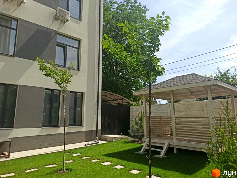 Зовнішній вигляд клубного будинку „На Генерала Пушкіна“ з прибудинковою територією: газон, дерева та альтанка.