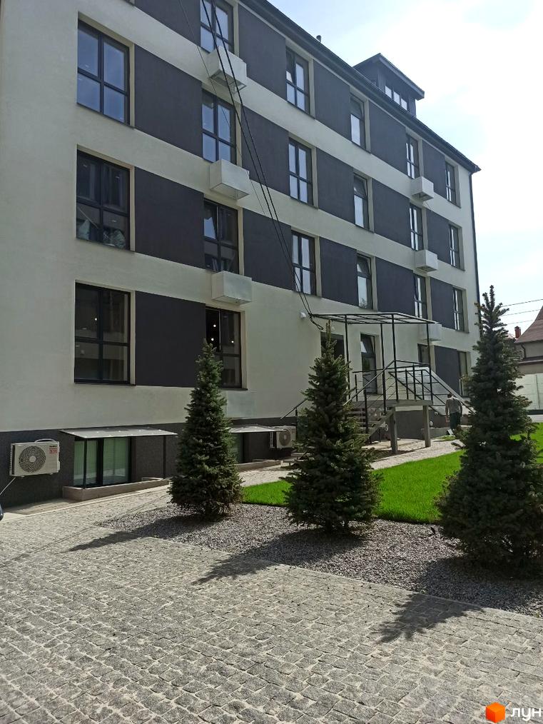 Зовнішній вигляд Клубні будинки „На Генерала Пушкіна“ з деревами на прибудинковій території та тротуарною плиткою.