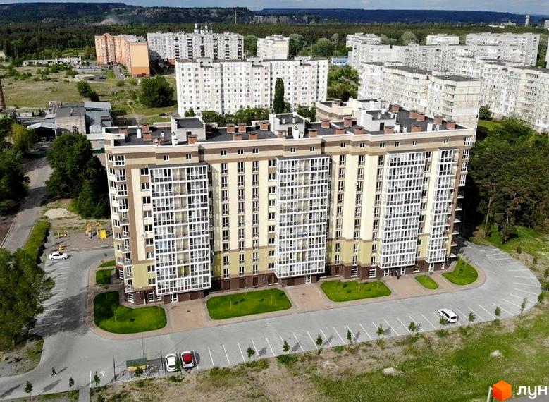 Житловий комплекс Oliva: багатоповерховий будинок світлих відтінків з великими вікнами та прибудинковою територією, що включає паркінг і зелені насадження.