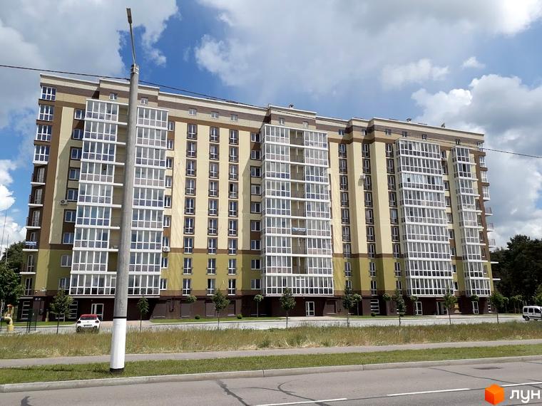 Житловий комплекс Oliva: багатоповерховий будинок зі світло-жовтим та зеленим фасадом, великими вікнами та заскленими балконами. Перед ним дорога та зелені насадження.