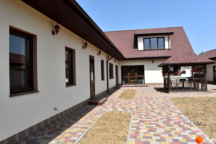 КК Містечко Здоров'я. Зовнішній вигляд будинку з коричневим дахом та білими стінами, з доріжкою з кольорової плитки та альтанкою.