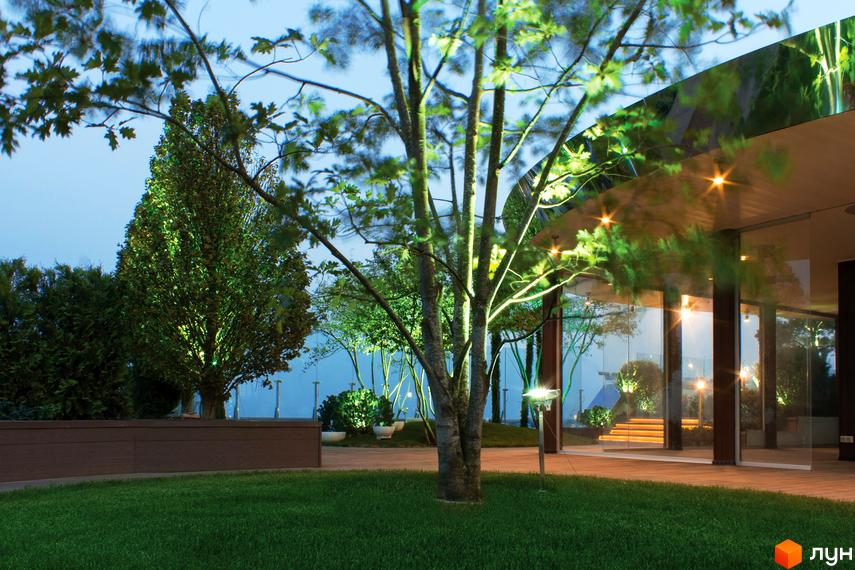 Житловий комплекс Royal Tower з панорамними вікнами та підсвіченими деревами на території. На подвір'ї газон та декоративні рослини.