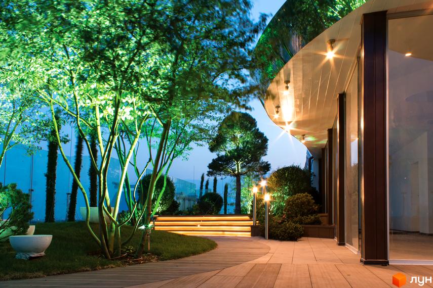 Житловий комплекс Royal Tower з панорамними вікнами та підсвіченою прибудинковою територією. На території комплексу висаджені дерева та кущі, облаштовані доріжки.