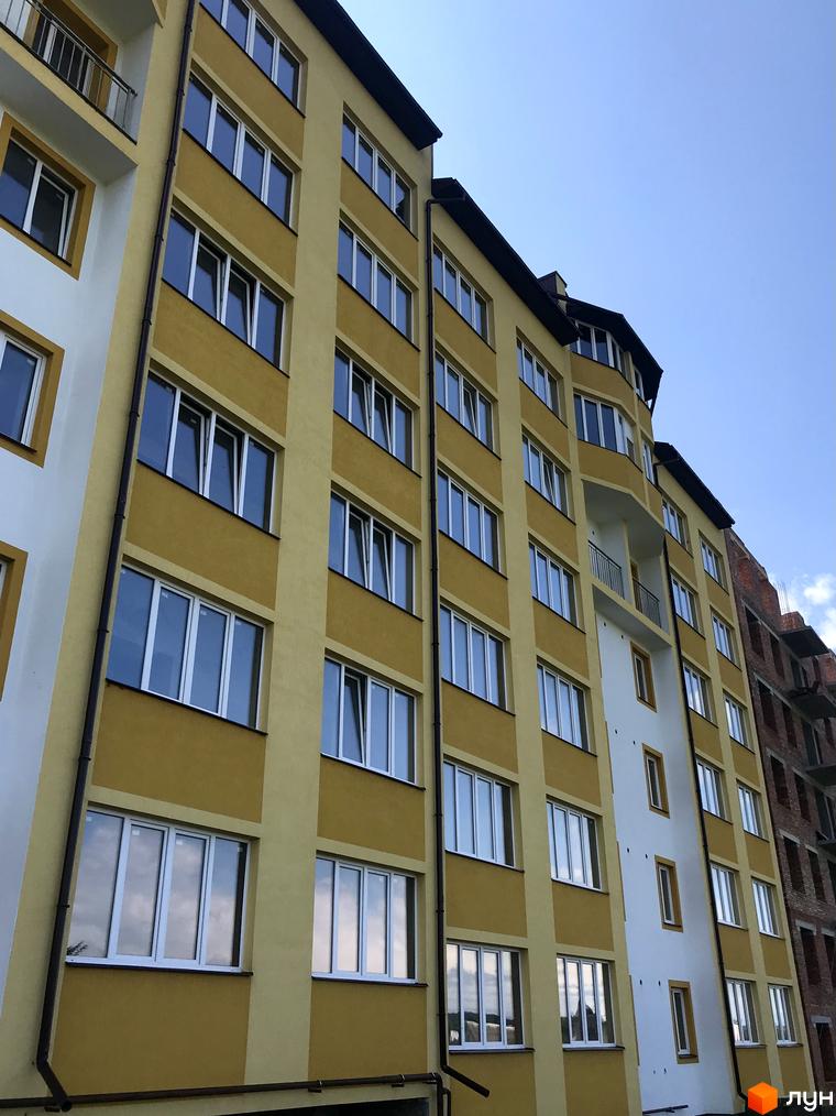 Зображення фасаду Житлового комплексу Світанковий. Багатоповерховий будинок з жовтими стінами та великими вікнами на фоні блакитного неба.