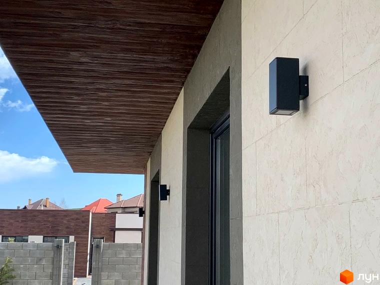 Зовнішній вигляд будинку в Котеджному містечку La Vida з освітленням на стіні. Вигляд на частину фасаду та дах будинку.