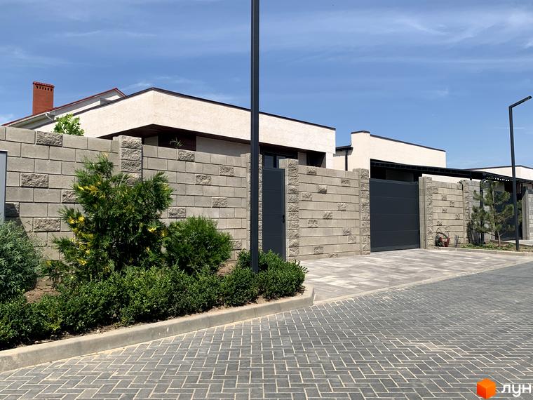 Зовнішній вигляд Котеджного містечка La Vida: цегляний паркан, зелені насадження, дорога з тротуарної плитки. Будинки з білим фасадом та червоним дахом.